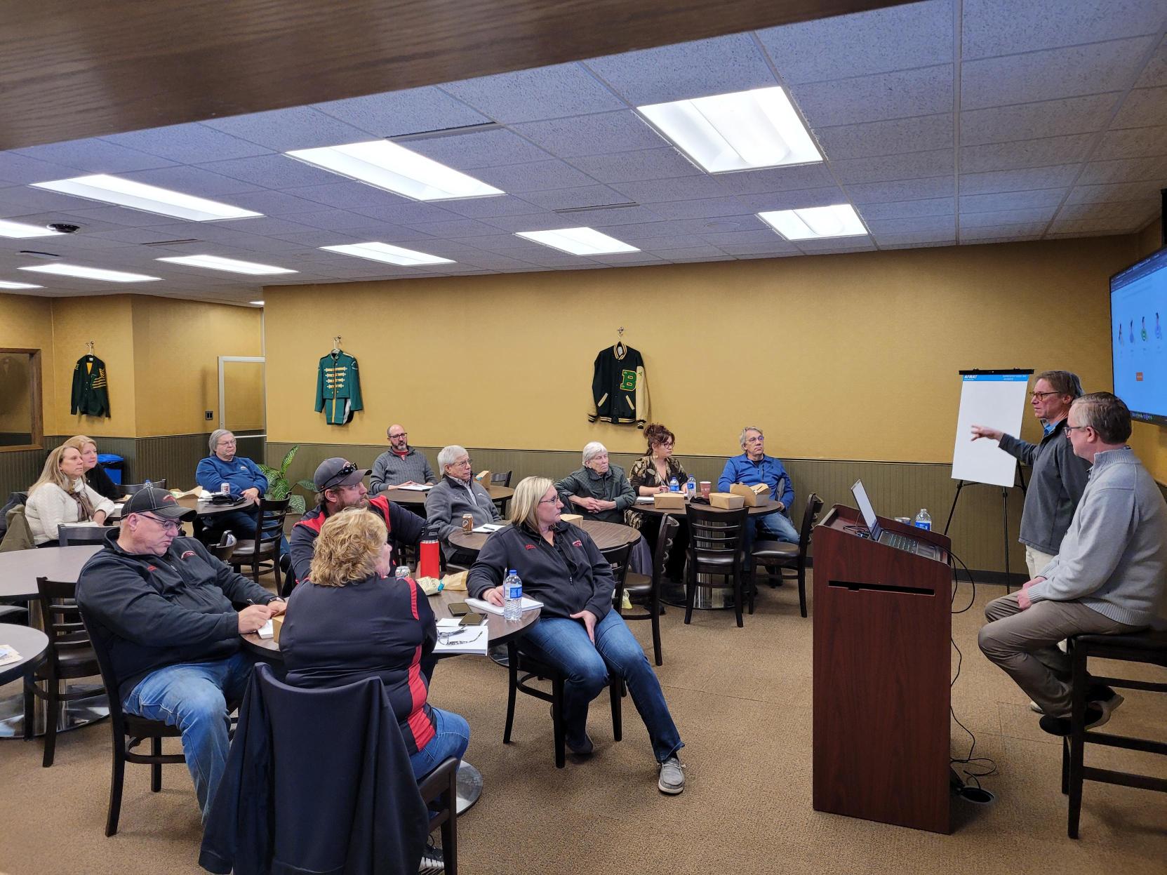 Two presenters speaking to a group seated at tables during a lunch and learn event